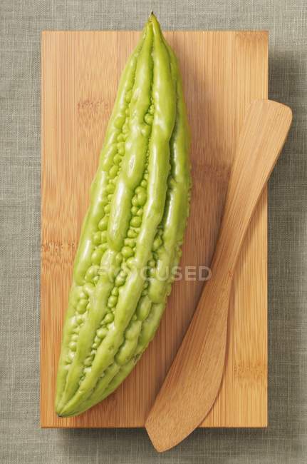 Closeup top view of one whole bitter melon with wooden knife on board — Stock Photo