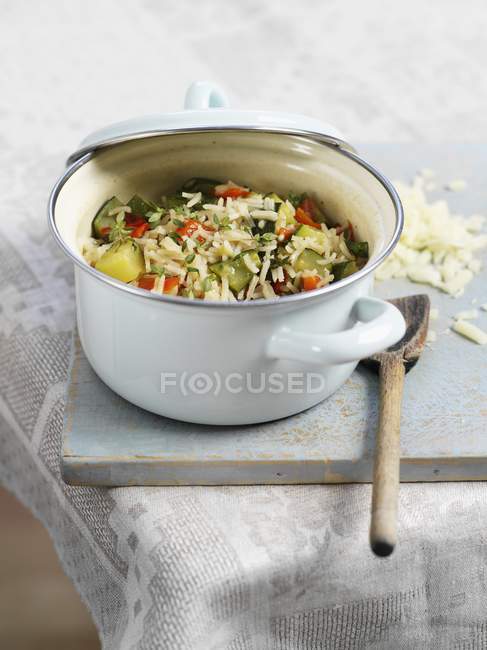 Vegetable risotto in a casserole dish over wooden desk with wooden spoon — Stock Photo