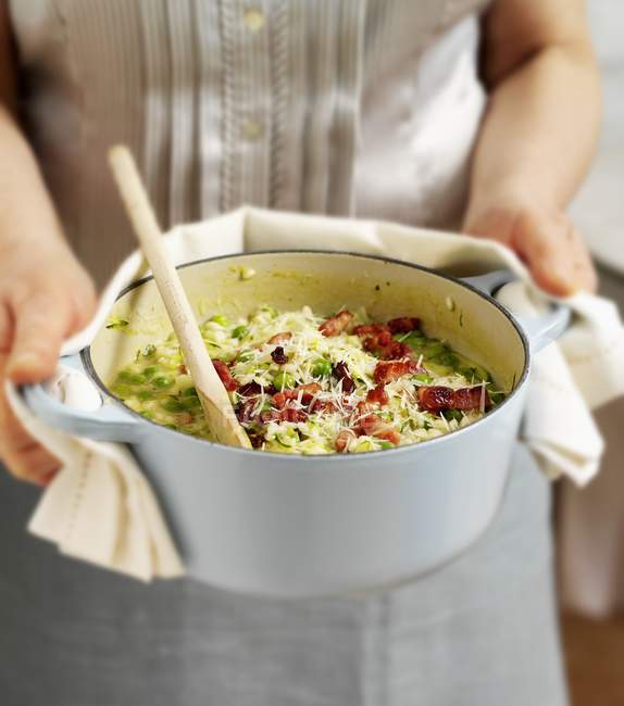 A woman holding a casserole pot full of courgette and pea risotto in hands, midsection — Stock Photo