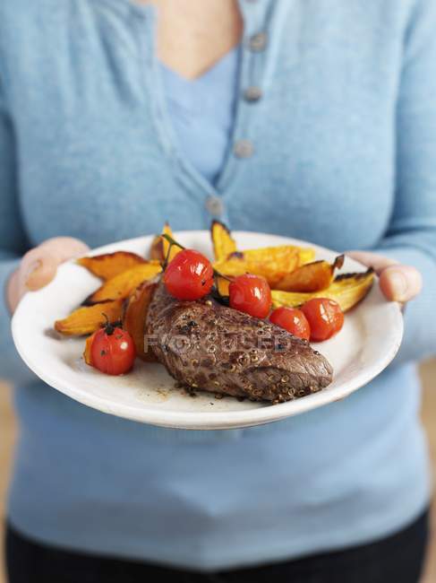 Woman holding plate of beef steak — Stock Photo