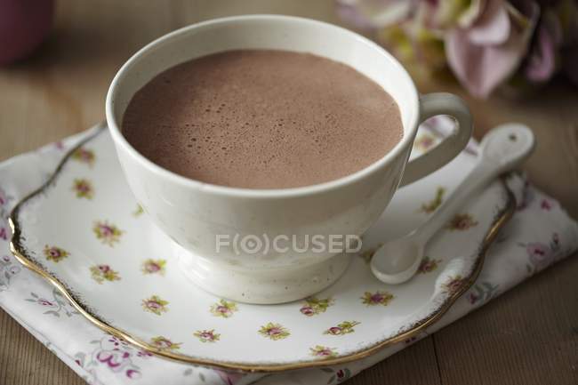 Vista de primer plano del cacao en taza blanca con cuchara en platillo estampado floral y servilleta - foto de stock