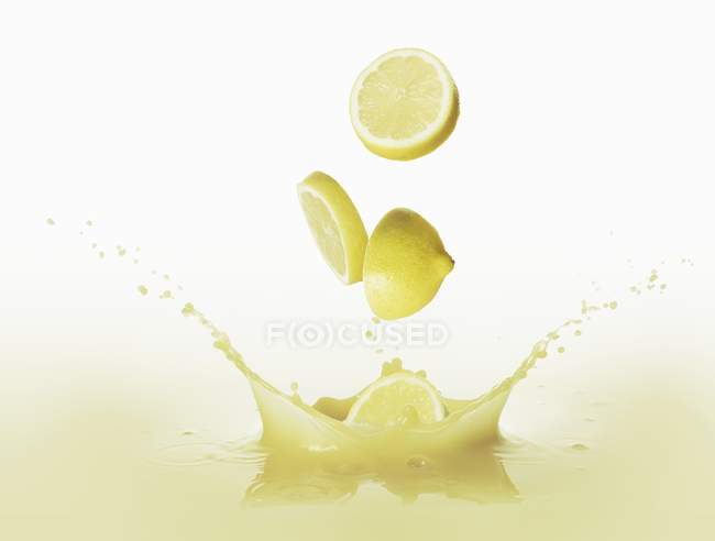 Limones cayendo en jugo de limón - foto de stock