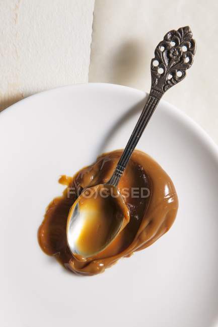 Closeup top view of Dulce de leche caramelised milk with spoon on white plate — Stock Photo