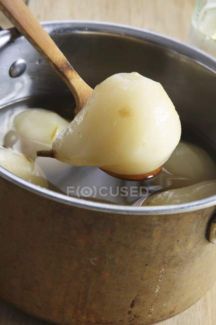 Poached pears in metal pot with wooden spoon over wooden surface — Stock Photo