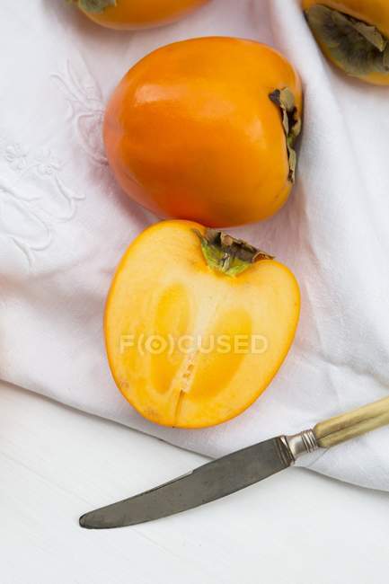Whole and halved Persimions with knife — Stock Photo