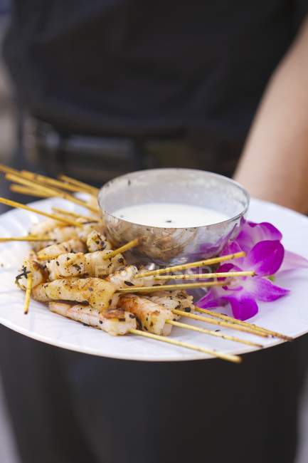 Closeup cropped view of person holding platter of shrimp skewers with yogurt dip — Stock Photo