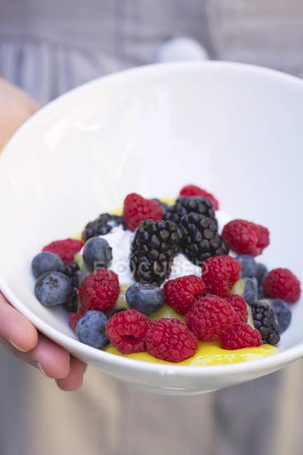Closeup cropped view of hand holding bowl of lemon curd, berries and whipped creme — Stock Photo