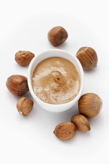 Closeup view of hazelnut paste and hazelnuts on white surface — Stock Photo