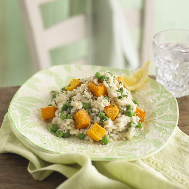 Risotto with peas and butternut squash on green plate over towel over wooden surface — Stock Photo