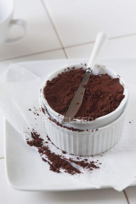 Vue rapprochée de la poudre de cacao dans un bol blanc avec couteau — Photo de stock