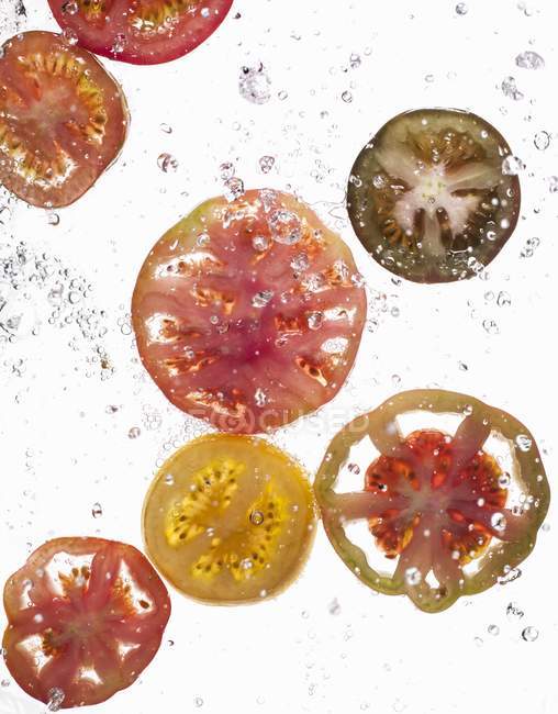 Slices of tomatoes falling in water — Stock Photo
