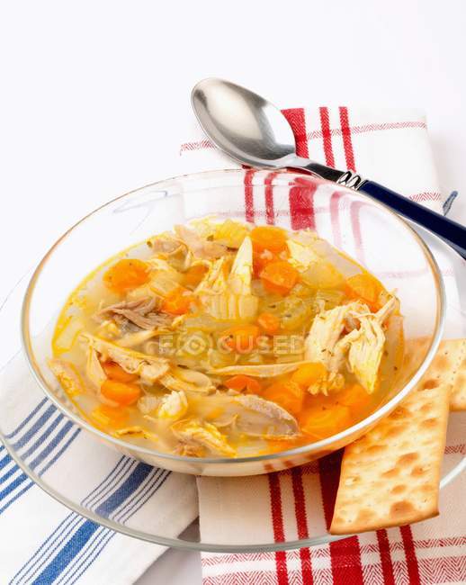Chicken and vegetable soup on glass plate over towel with spoon — Stock Photo