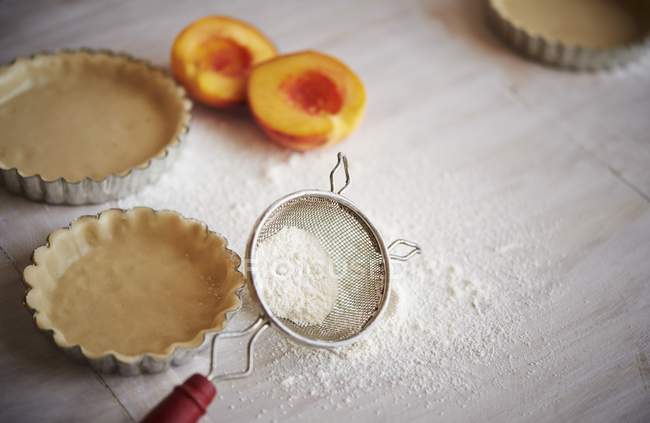 Closeup view of tart pans with pastry, fresh peaches and flour — Stock Photo