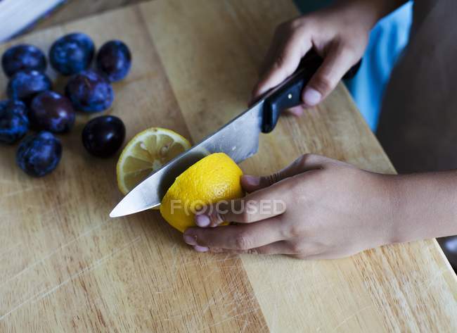 Niño cortando limón por la mitad con cuchillo - foto de stock