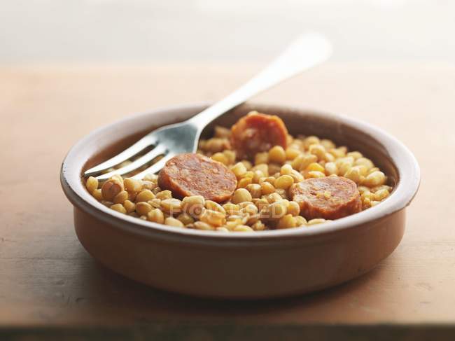 Closeup view of lentils with Chorizo sausage pieces and fork in a bowl — Stock Photo