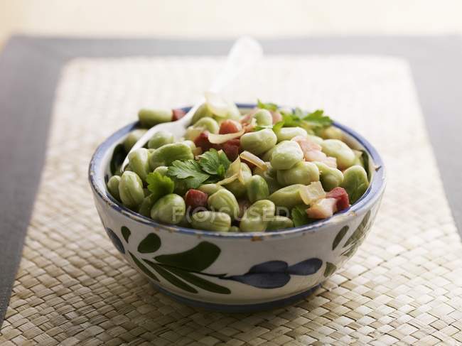 Broad bean and ham in bowl over straw mat — Stock Photo