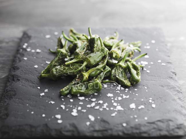 Padron Peppers and rock salt on black surface — Stock Photo