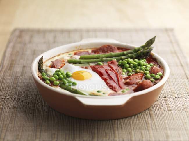 Baked eggs red pepper asparagus peas and chorizo in platter over textile surface — Stock Photo