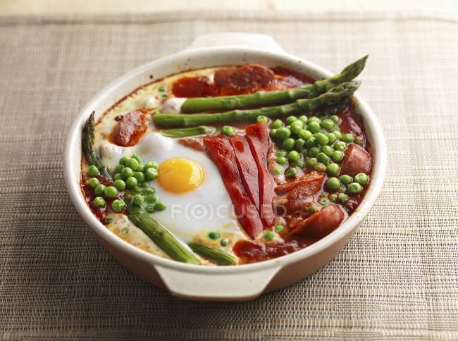 Baked eggs red pepper asparagus peas and chorizo in white dish — Stock Photo
