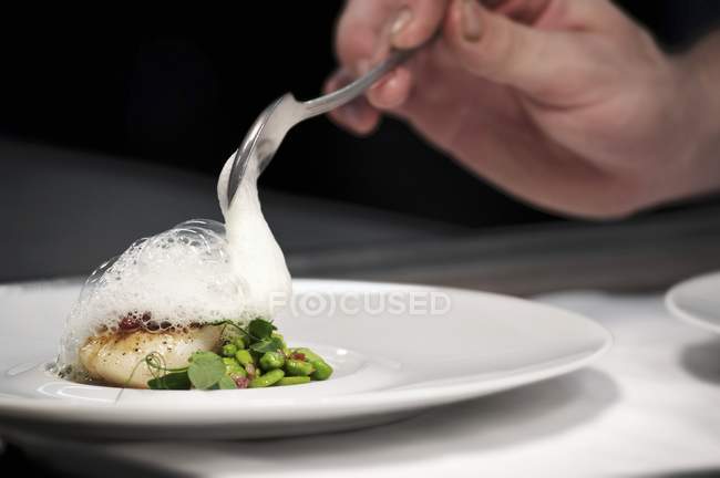 Chef plating up fish and broad bean dish during service at working restaurant — Stock Photo