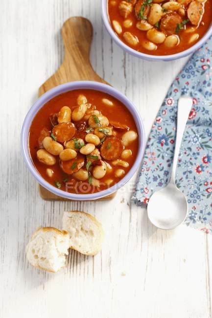 Beans with sausage and bacon in tomato sauce over wooden surface — Stock Photo