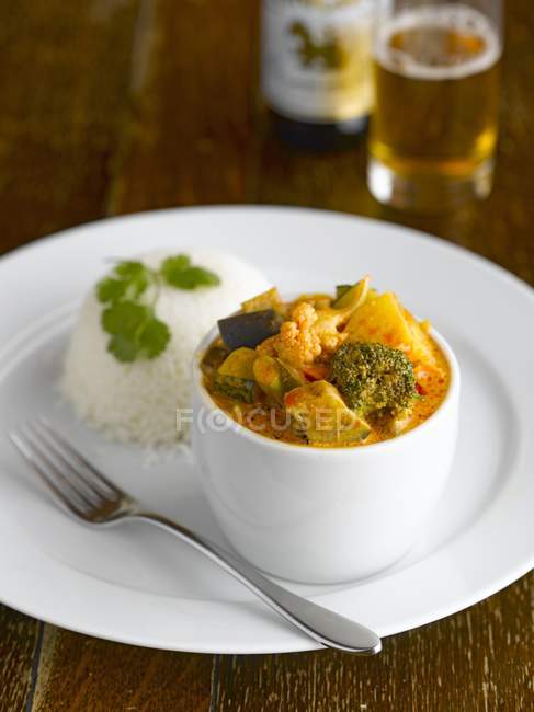 Curry tailandese su piatto bianco con piattino e forchetta su superficie in legno — Foto stock