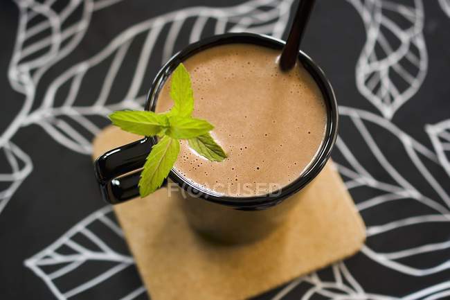 Closeup view of cocoa in a black cup with a straw and a mint garnish — Stock Photo