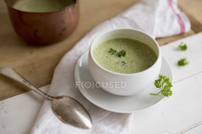 Cream of broccoli soup in white bowl over towel with spoon — Stock Photo