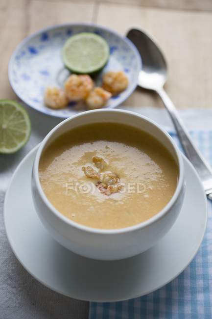 Prawn and coconut soup with limes in bowl over small plate — Stock Photo