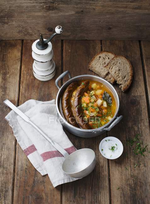 Vista elevada de la sopa de calabaza y patata con salchichas y pan - foto de stock