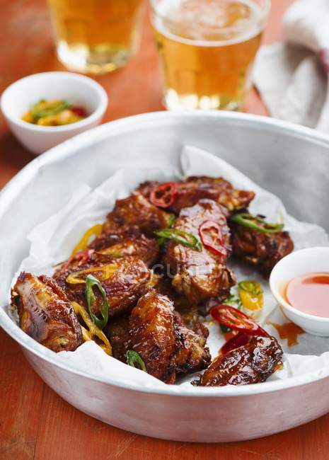 Ali di pollo con salsa al peperoncino e birra in piatto sopra il tavolo — Foto stock