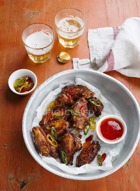 Ali di pollo con salsa di peperoncino e birra su piatto bianco su superficie di legno — Foto stock
