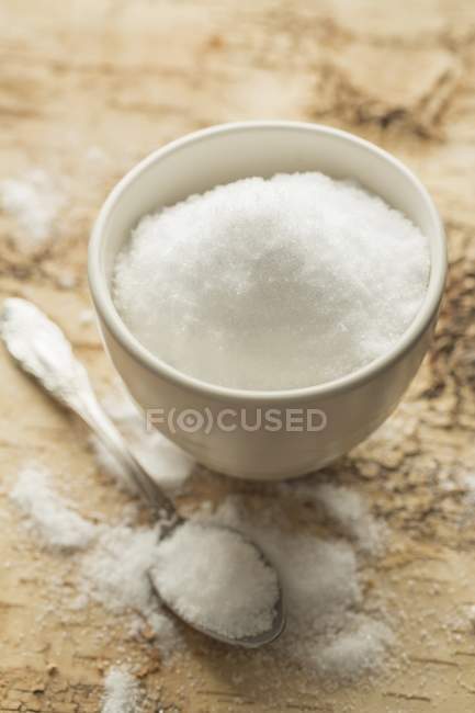 Closeup view of Xylitol in white bowl with spoon on a bark surface — Stock Photo