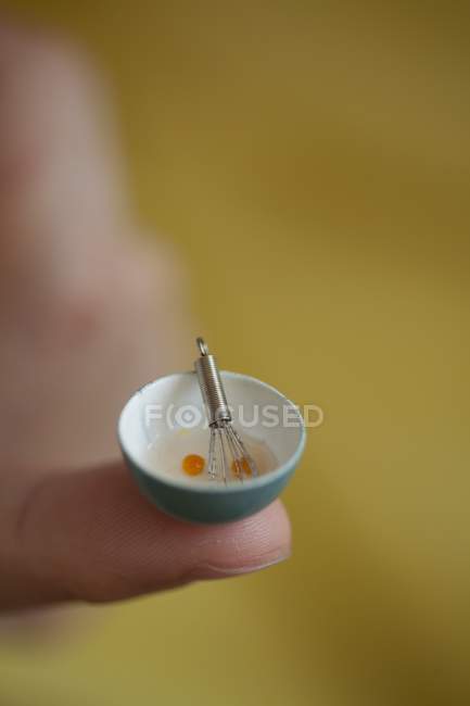Vista de primer plano de un tazón minúsculo de huevos batidos en la punta de un dedo - foto de stock
