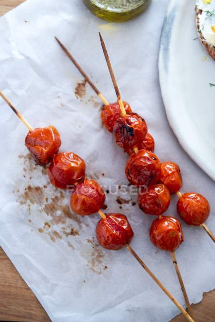 Tomates cherry asados en palos de madera sobre toalla blanca - foto de stock