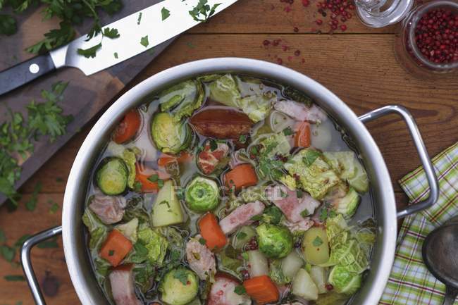 Vegetable stew with ham and bacon in pan over wooden surface — Stock Photo