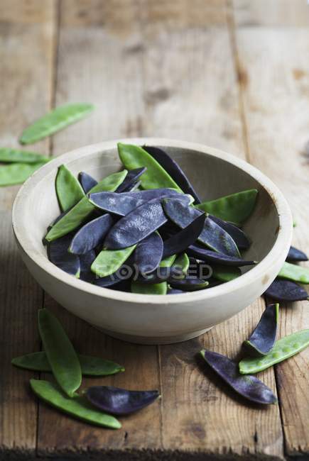 A bowl of green and purple mange tout in bowl over wooden surface — Stock Photo