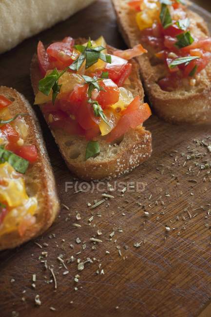 Bruschetta topped with basil and seasonings on a wooden surface — Stock Photo