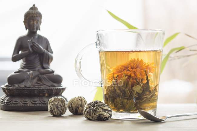 Стакан цветочного чая и фигурка Будды — стоковое фото
