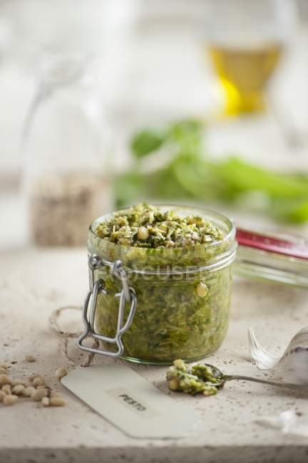 Closeup view of an opened jar of fresh basil pesto surrounded by ingredients — Stock Photo