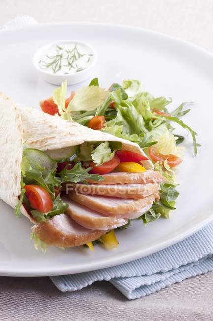 Una envoltura con pollo ahumado y verduras en un plato blanco sobre una toalla - foto de stock