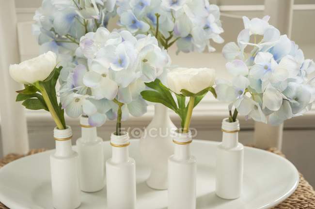 Hydrangeas and buttercups in white painted vases and bottles — Stock Photo