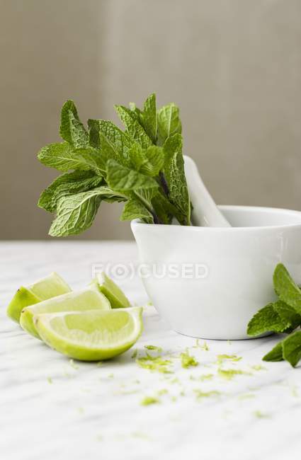 Mint in mortar with lime wedges — Stock Photo