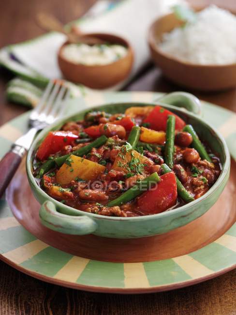 Five bean chilli in colored bowl over plate with fork — Stock Photo