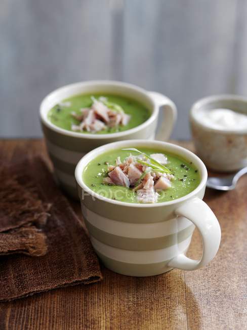 Cream of pea soup with ham in cups over wooden surface — Stock Photo