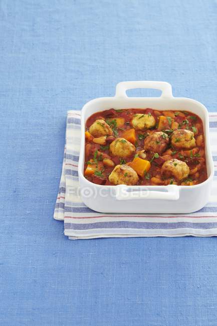A bake with small dumplings, tomatoes, sweet potatoes and parsley in white dish over towel — Stock Photo