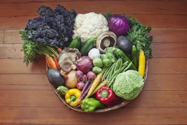 A basket of vegetables on a wooden surface on brown plate over wooden surface — Stock Photo