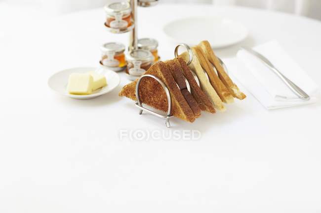 Підвищений вид на тости в тостній стійці, що подається з маслом і різними баночками варення — стокове фото
