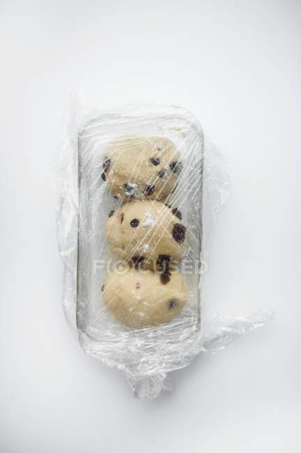 Closeup top view of raw dough pieces with fruit in baking dish covered with clingfilm — Stock Photo