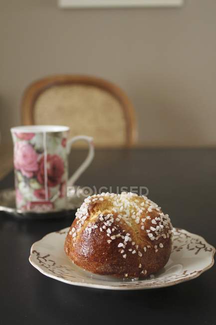 Closeup view of Brioche with sugar nibs and tea in a floral-patterned mug — Stock Photo